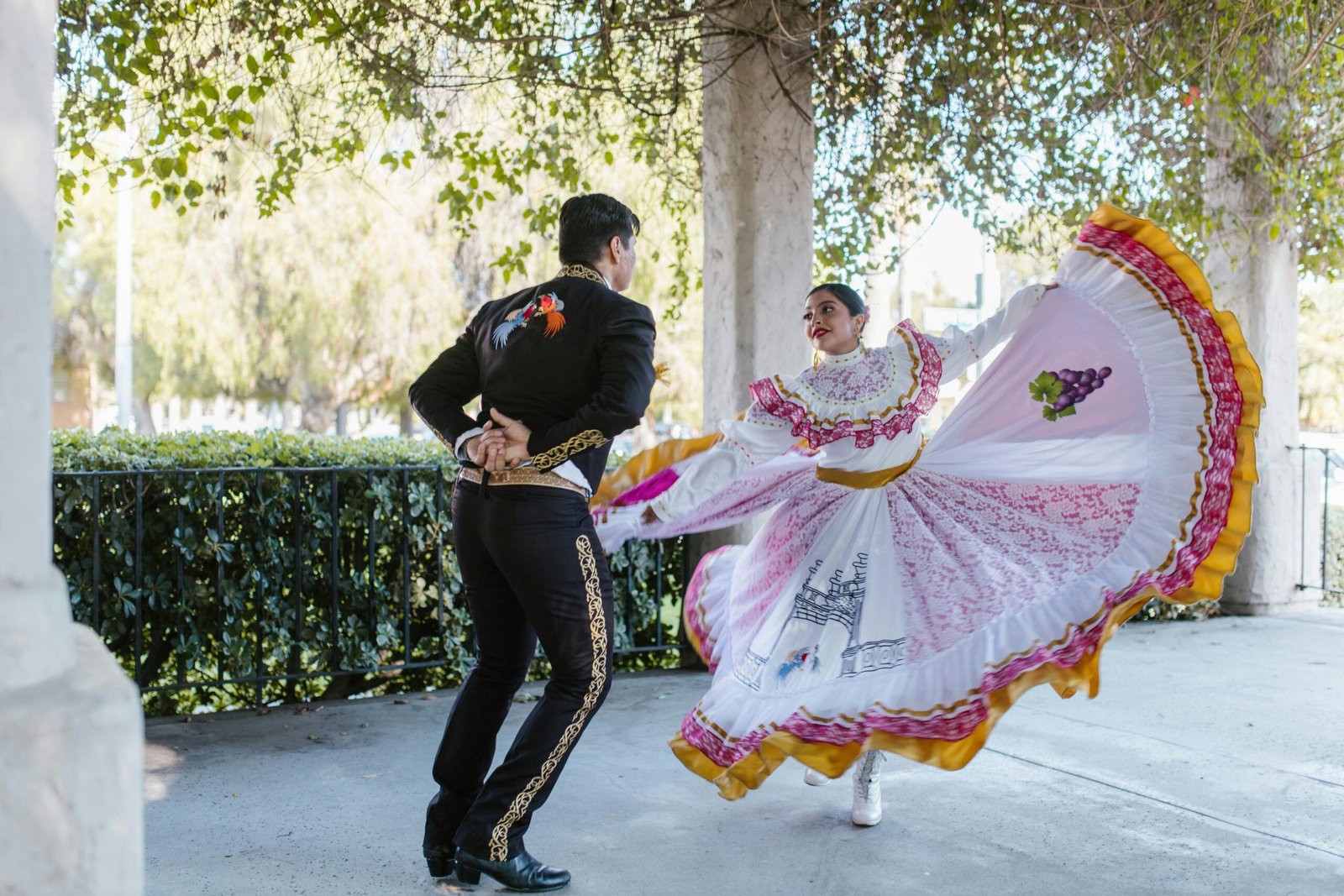 A couple performs traditional Mexican folk dance outdoors in vibrant costumes.